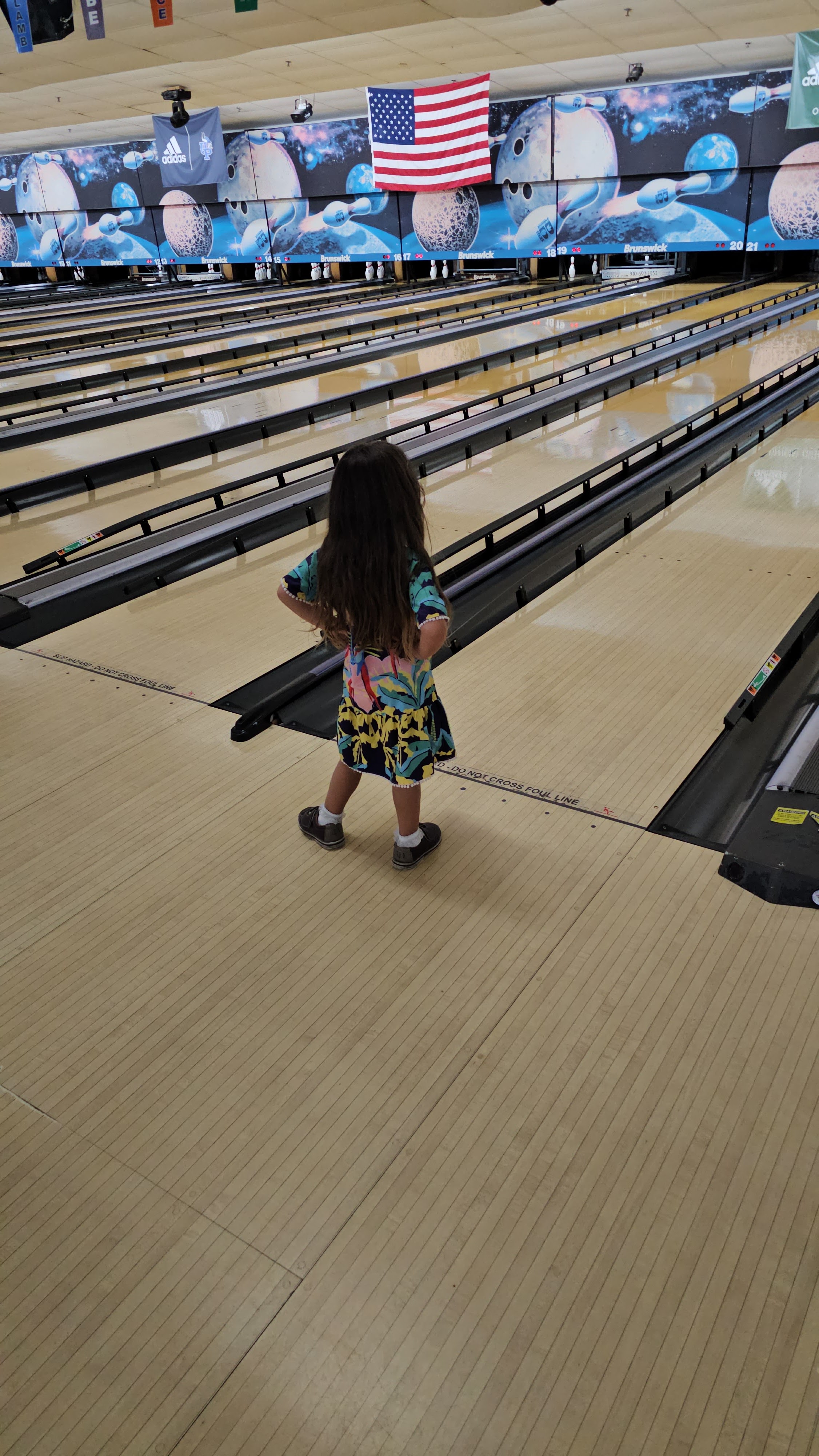 A young girl stands at the foul line of a bowling lane with bumpers up in a space-themed bowling center.