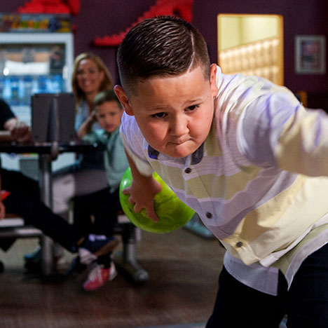 A young boy concentrates while preparing to throw a lime green bowling ball at a bowling alley.