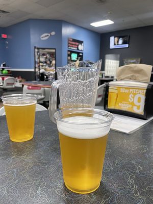 Two plastic cups and a pitcher of golden beer on a table with a bowling pin pattern.