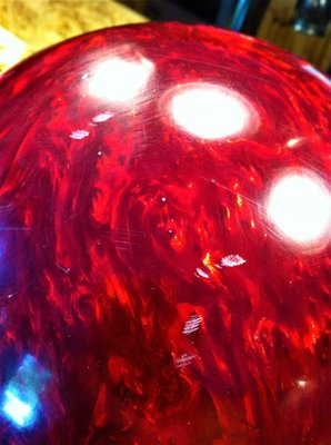 Close-up of a marbled red bowling ball with visible scratches and bright light reflections on its surface.
