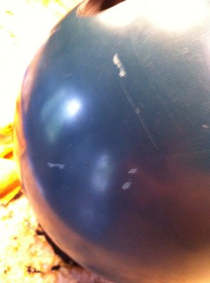 A close-up view of a scuffed blue bowling ball reflecting a bright light.