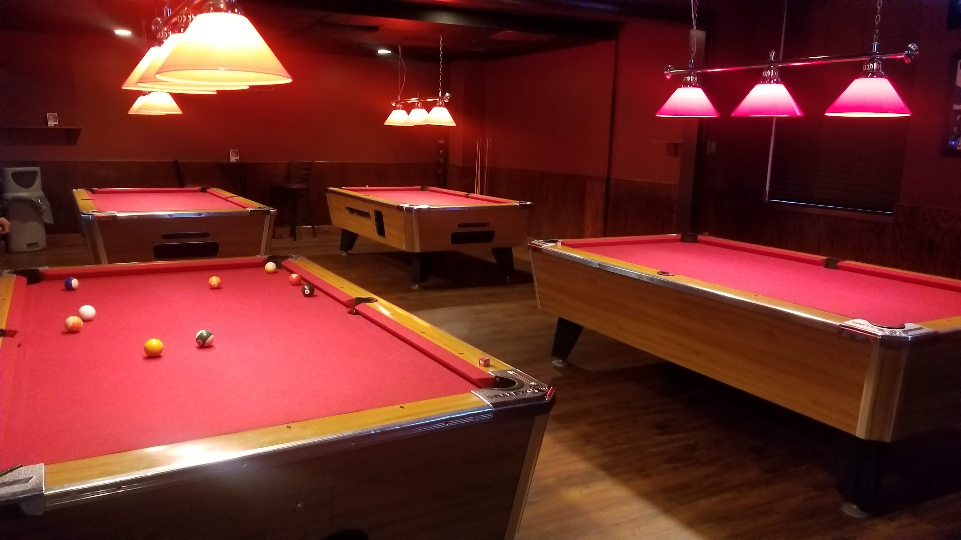 A room with four red felt pool tables under warm pendant lighting.