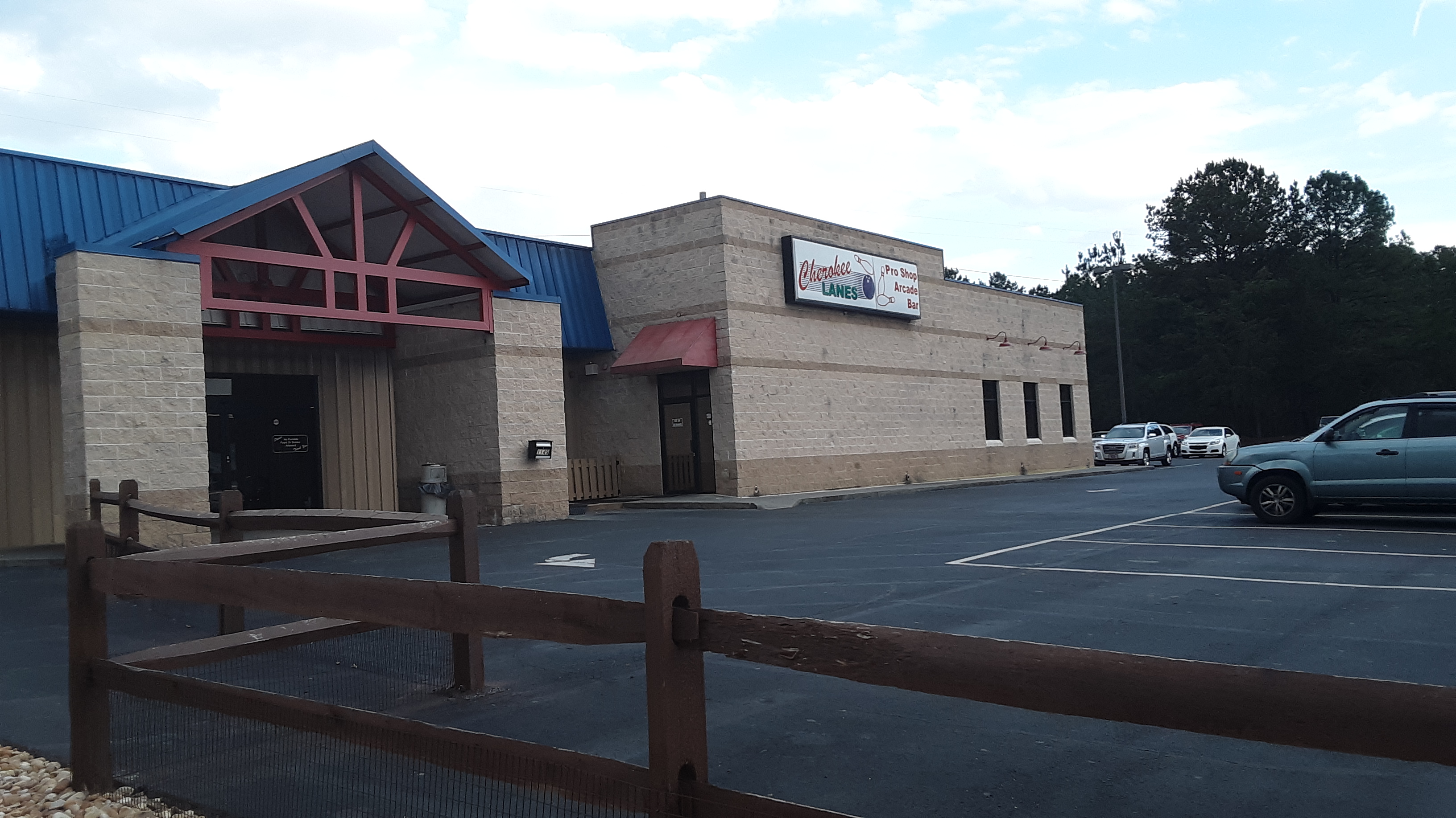 The exterior of Cherokee Lanes bowling center with a blue roof and a spacious asphalt parking lot.