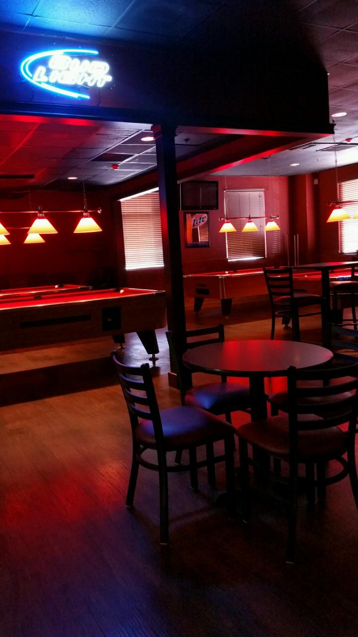 A dimly lit lounge area with red pool tables, dining seating, and a neon beer sign.