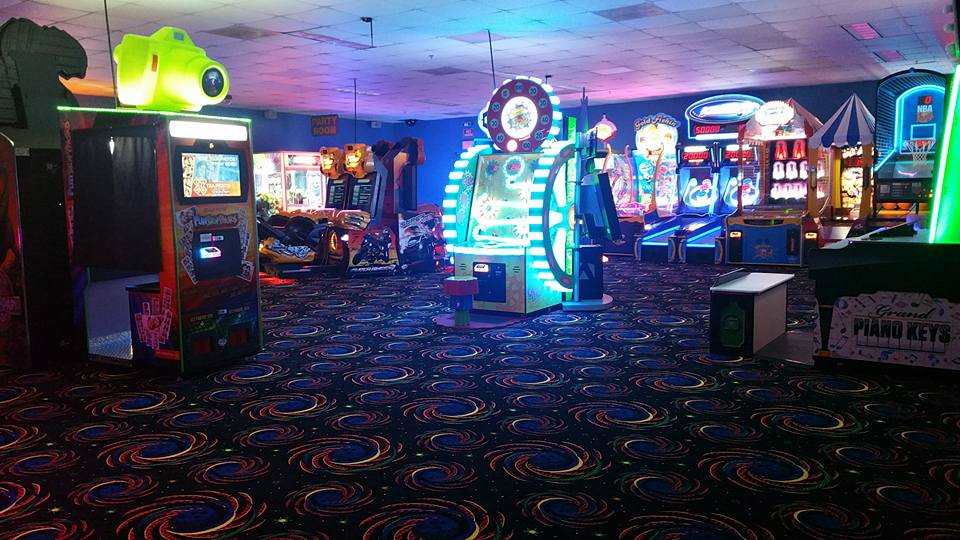 A brightly lit arcade room with colorful game machines and patterned carpet.