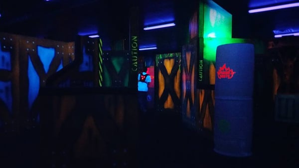 A dark laser tag arena with glowing neon barriers and a player wearing a lighted vest.