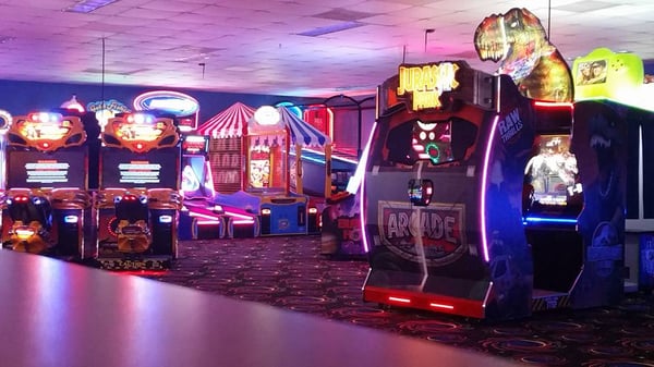 A modern bowling center arcade with glowing Jurassic Park and racing games under dim colorful lighting.