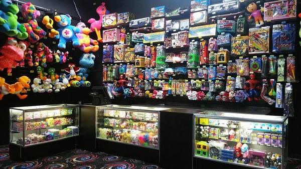 A colorful arcade prize redemption counter filled with stuffed animals, toys, and games in glass display cases.