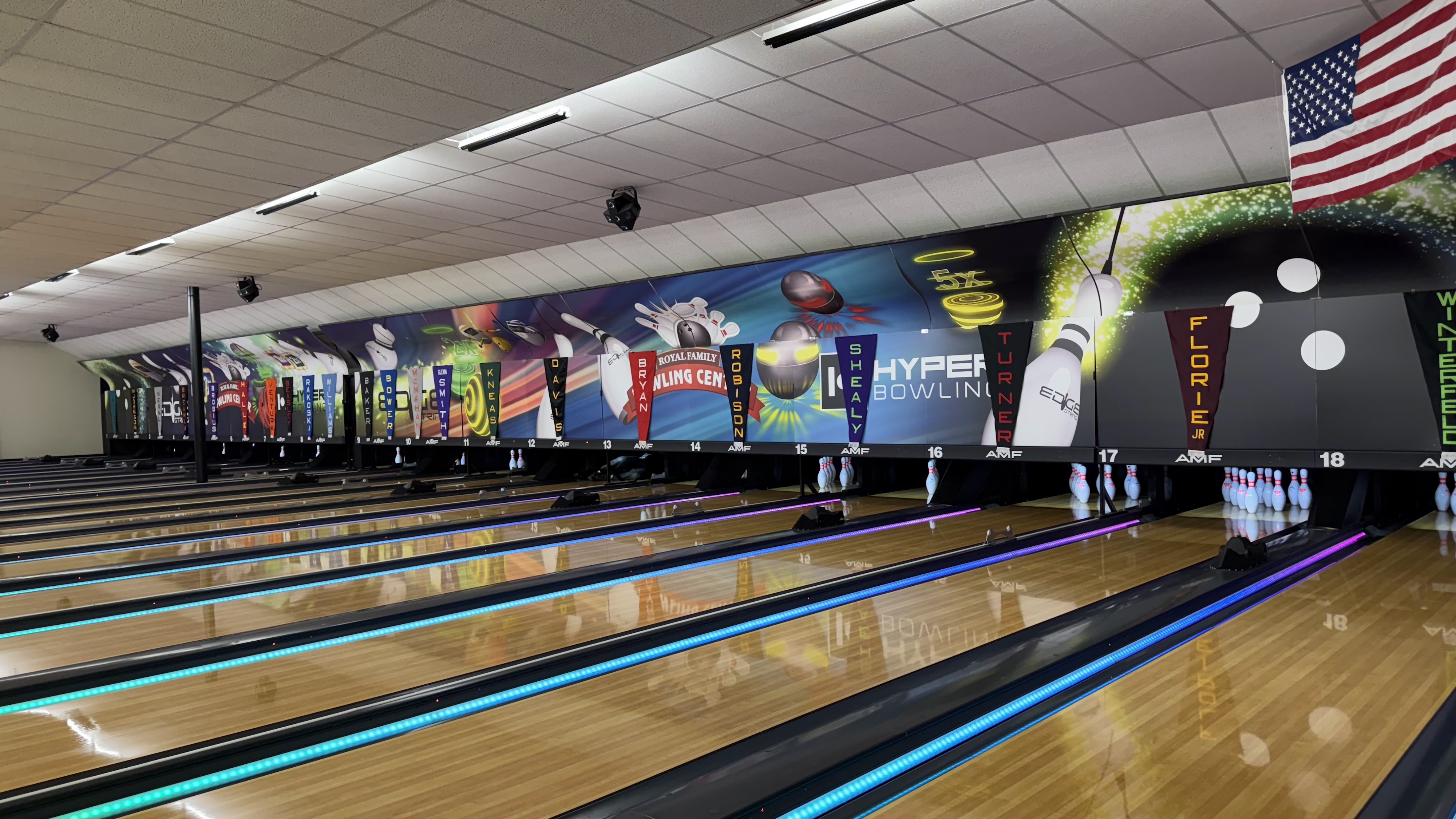 A wide view of polished bowling lanes with blue and purple LED lighting and cosmic-themed wall graphics.
