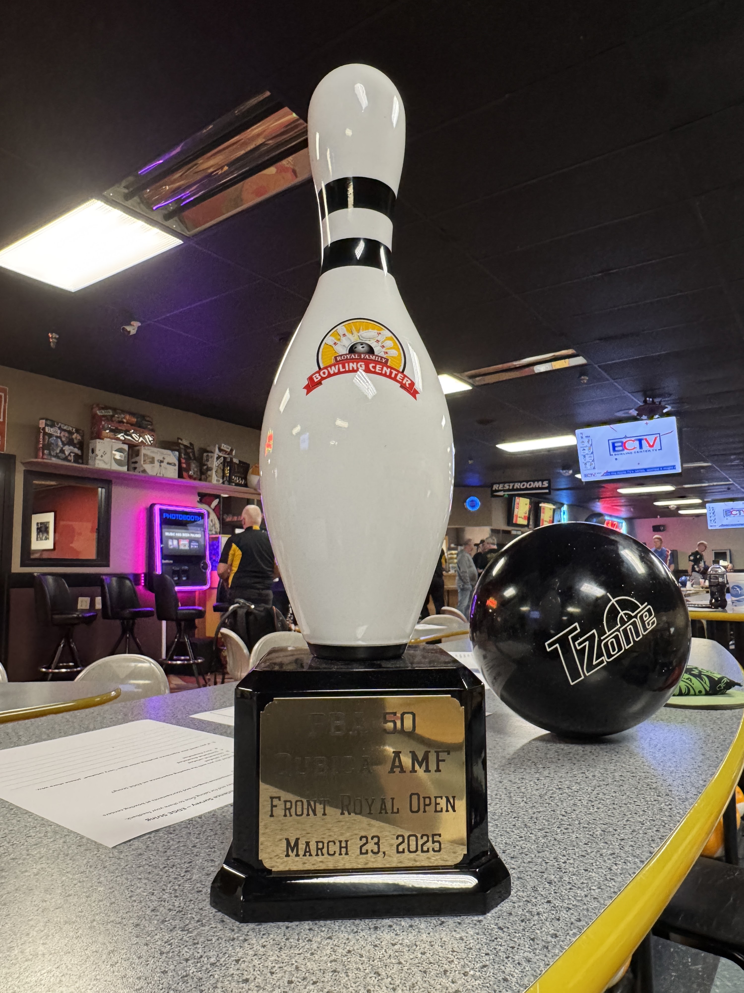 A bowling pin trophy for the Front Royal Open sits on a table next to a black TZone bowling ball.