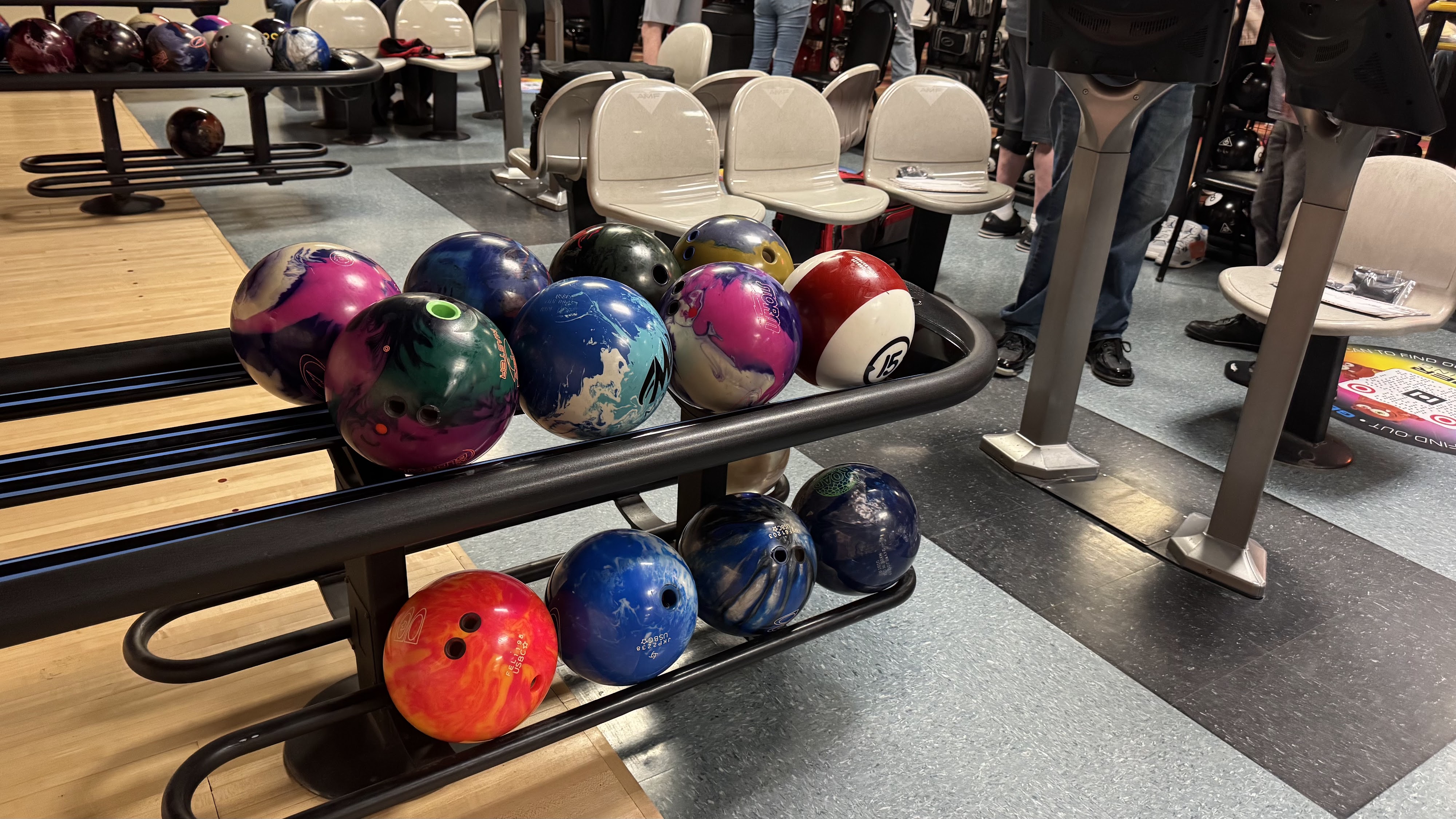 A two-tier rack filled with colorful bowling balls in the bowler's area of a bowling center.