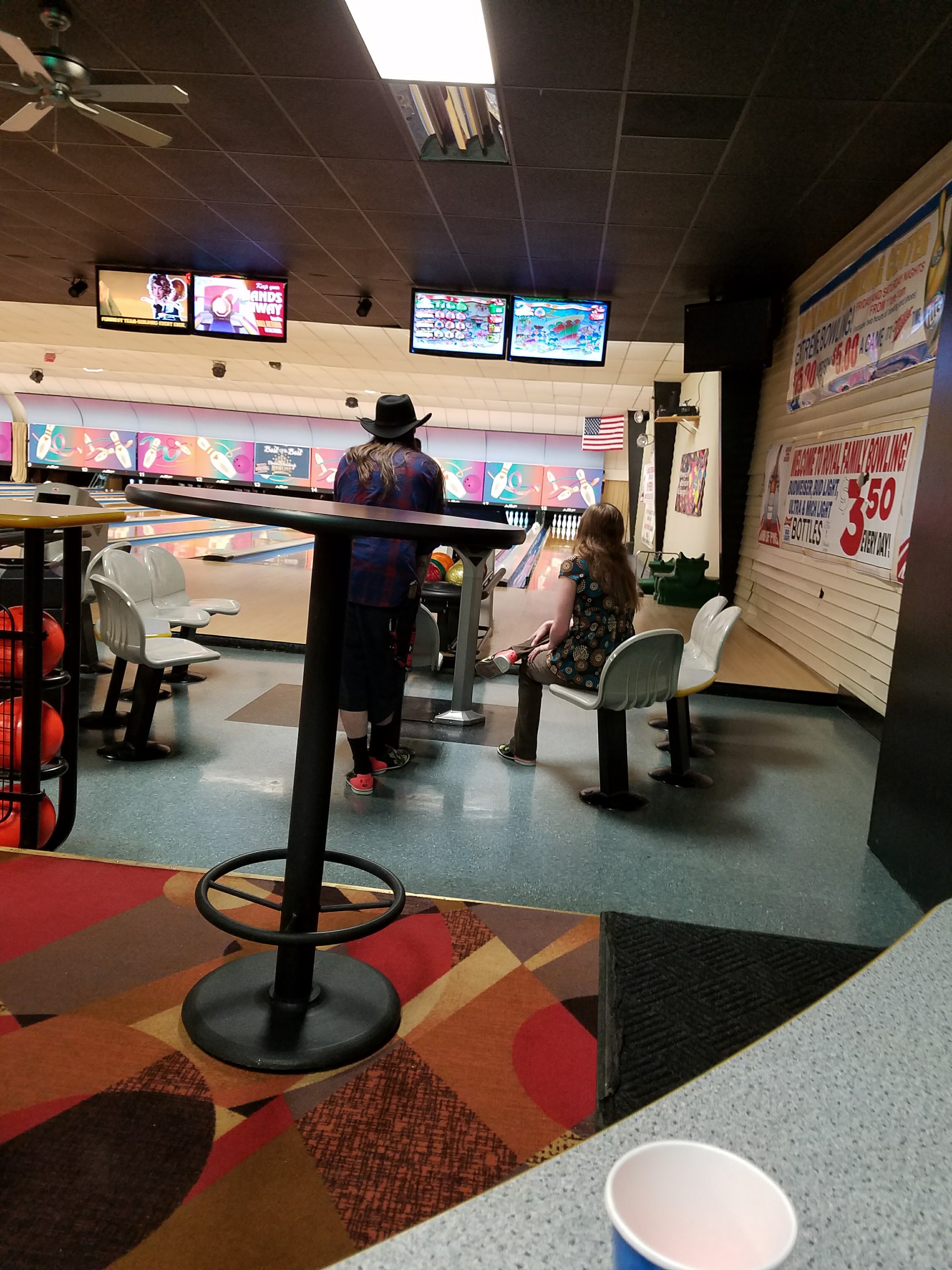 Interior view of a bowling center with patrons near the lanes and overhead scoring monitors.