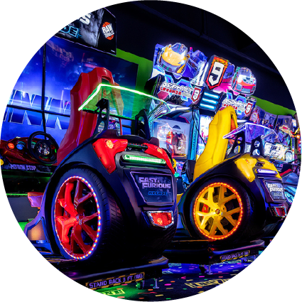 Two modern racing arcade games with vibrant neon lighting and glowing wheels in a dark game room.
