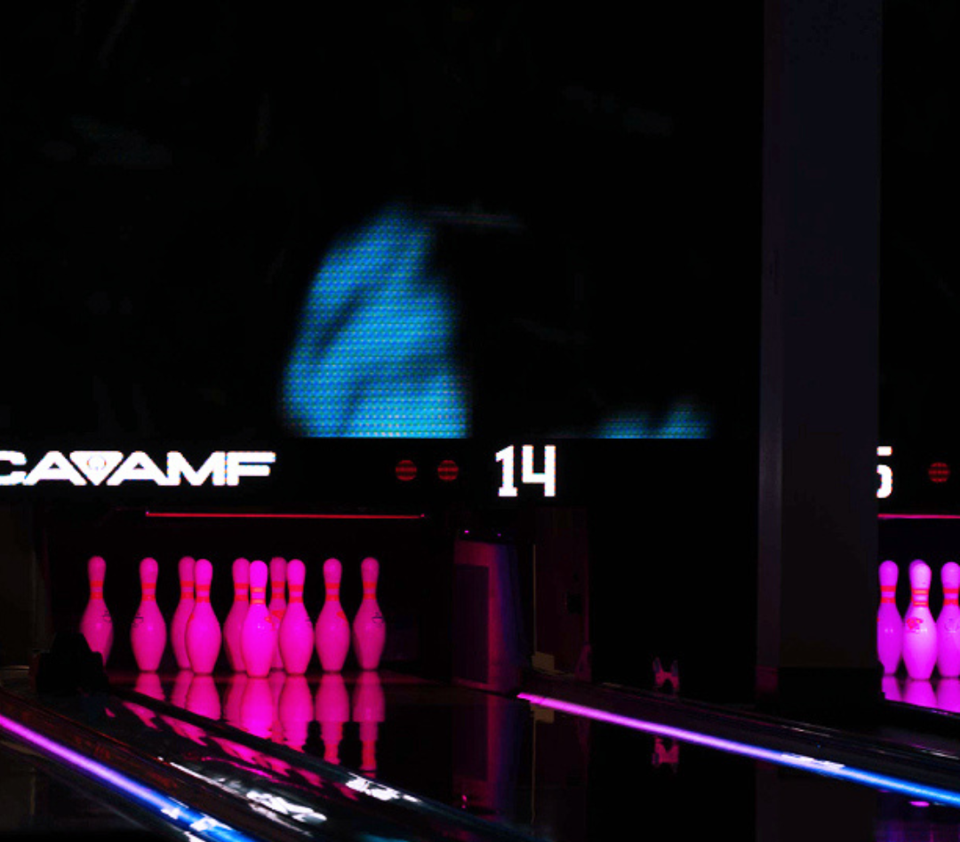 Bowling pins glowing magenta on lane 14 under cosmic neon lighting.