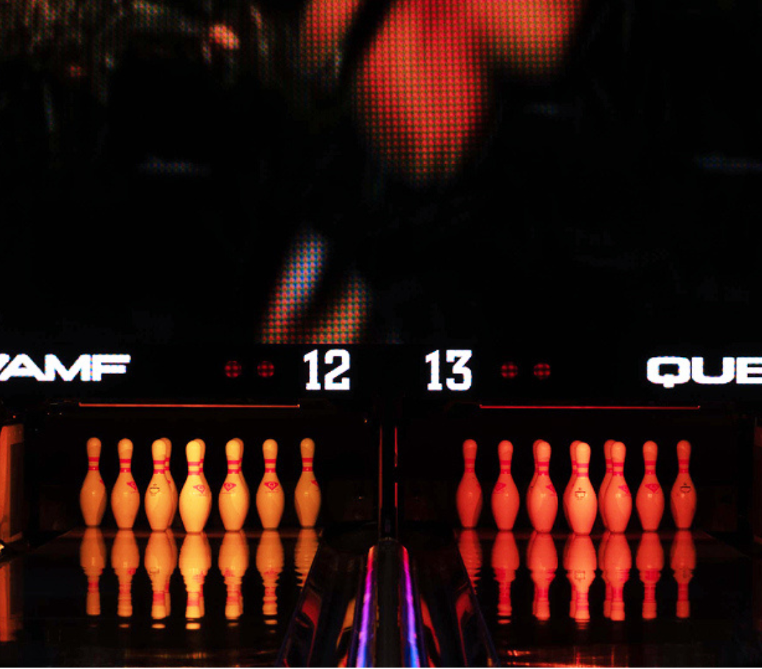 Bowling pins on lanes 12 and 13 under glowing red lights with reflections on the polished floor.