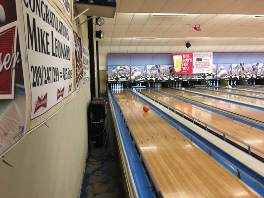 A series of bowling lanes with a high-score achievement banner on the side wall and an orange ball on the lane.