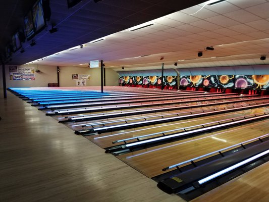 A wide view of several bowling lanes with glowing blue and white bumper lights in a modern bowling alley.
