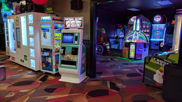 A modern bowling center arcade with glowing game machines, a prize cabinet, and a card kiosk on patterned carpet.