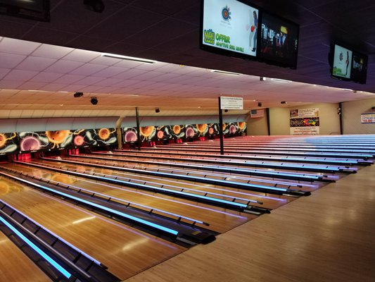Wide view of bowling lanes with blue glowing bumpers and cosmic themed backmasks.
