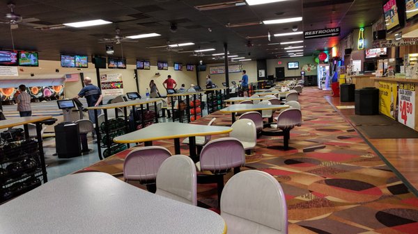 A wide interior view of a bowling alley showing seating areas, lanes, and overhead scoring monitors.