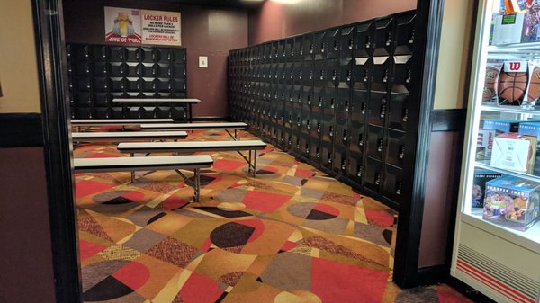 A clean locker room with black storage units, white benches, and a colorful geometric patterned carpet.