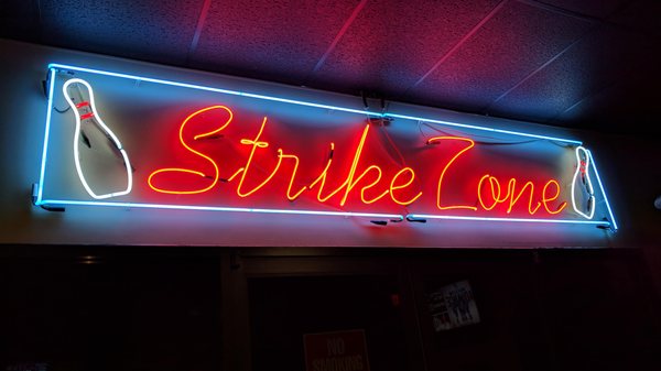 A red neon sign reading Strike Zone in cursive, framed by blue neon with two bowling pin icons.