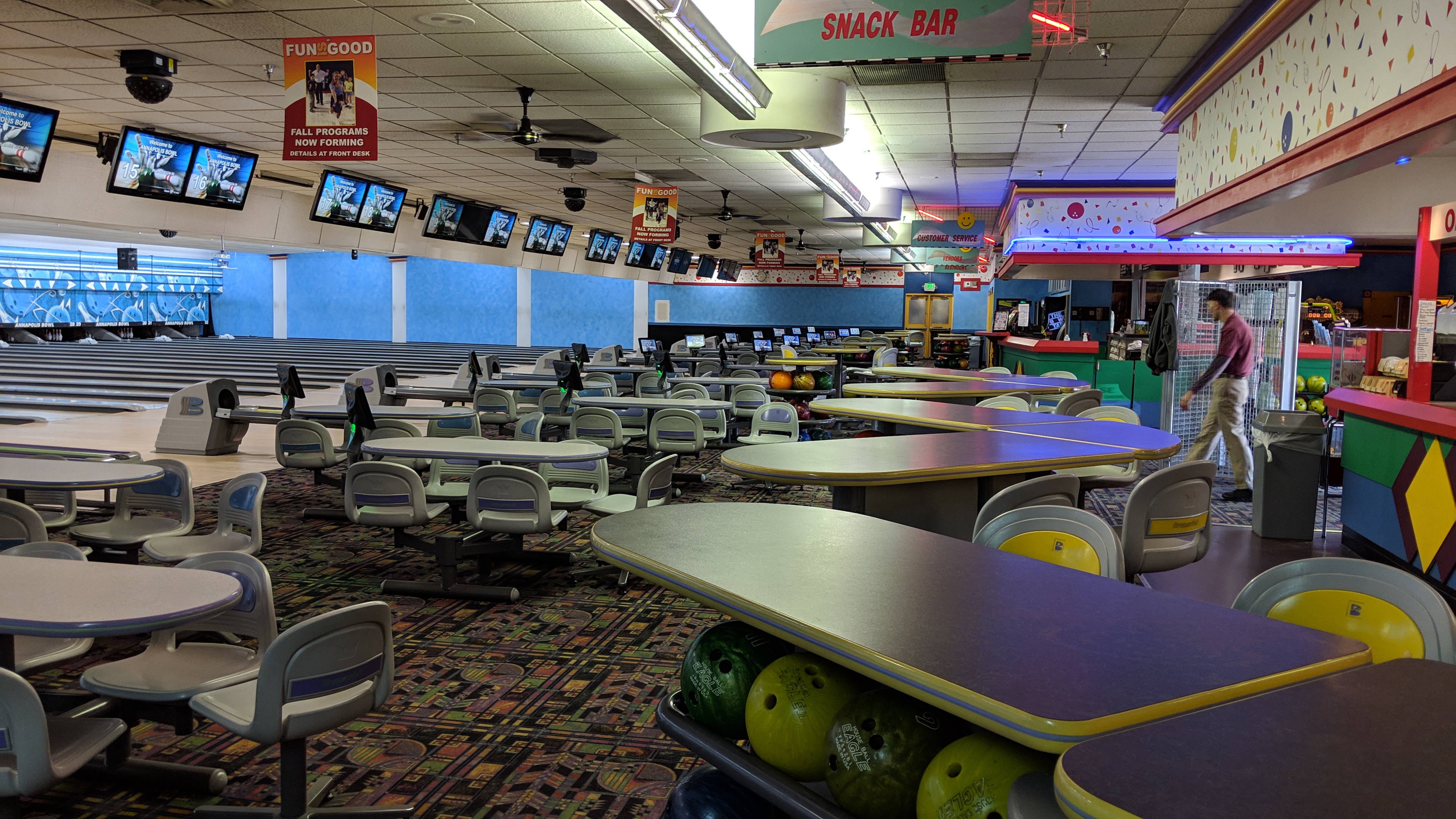 An expansive interior view of a bowling alley with rows of lanes, spectator seating, and a snack bar.