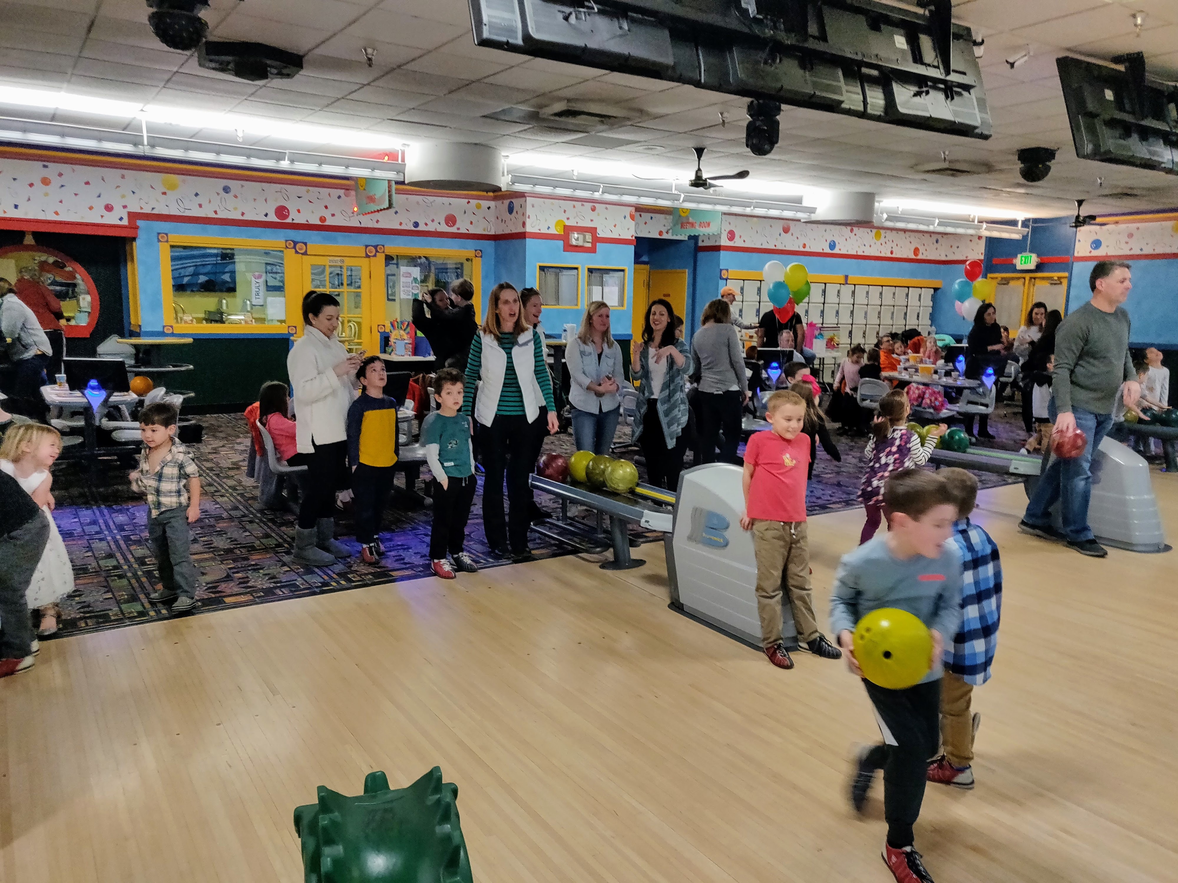 A group of children and adults enjoying a bowling party at a brightly lit indoor bowling center.