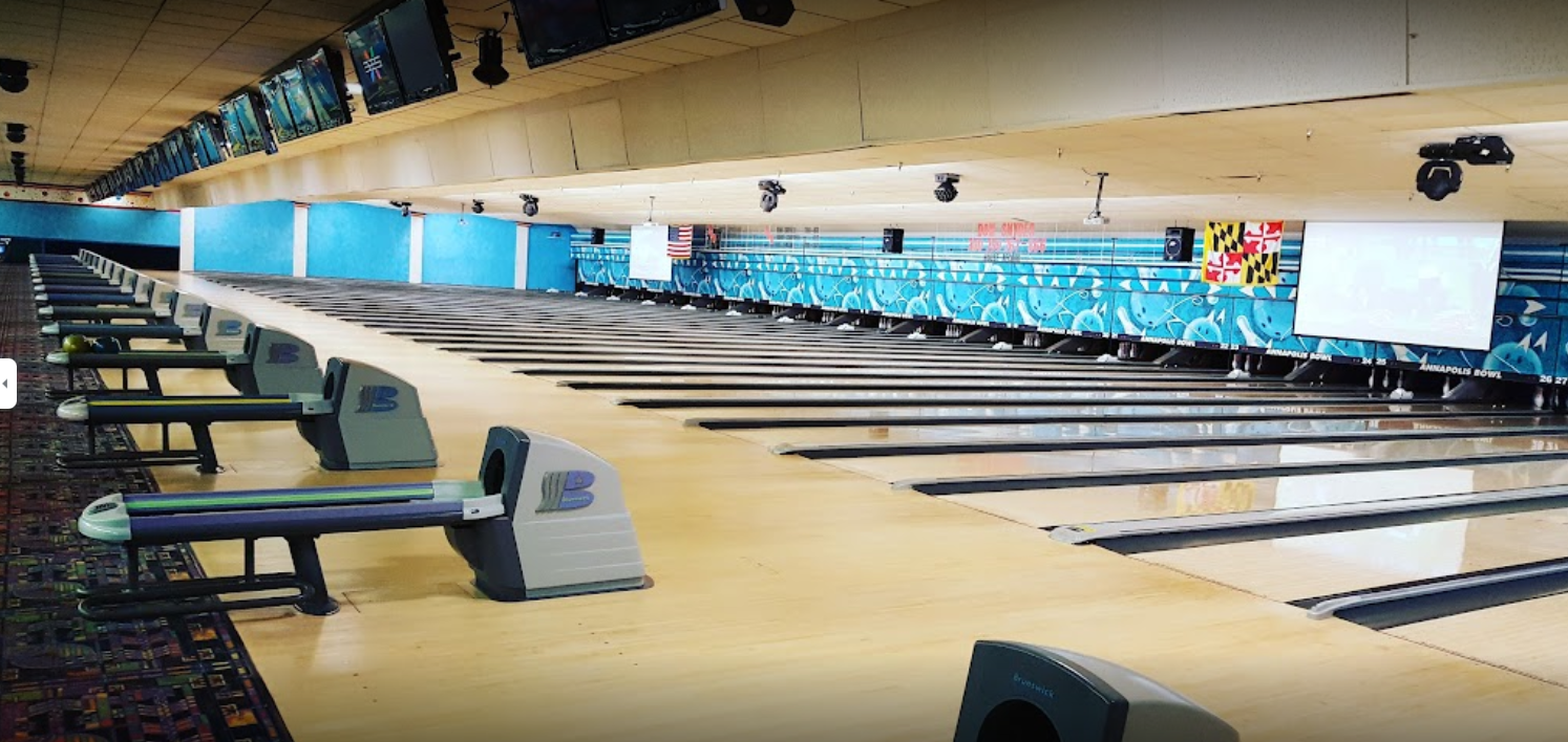 A wide view of a modern bowling alley with multiple lanes, overhead monitors, and blue-themed graphics.