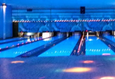 Bowling lanes glowing under vibrant blue cosmic lights with colorful patterns on the approach.