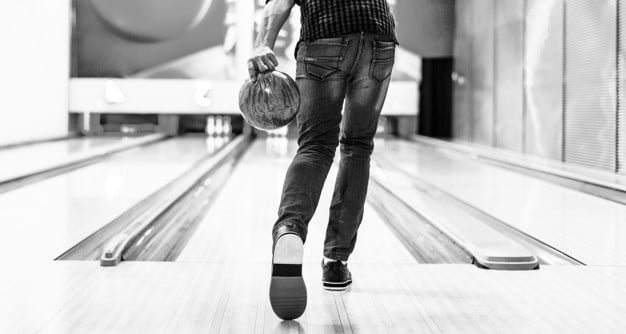 Black and white photo of a bowler from behind, holding a ball while standing on a lane.