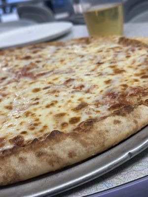 Close-up of a hot cheese pizza on a metal tray at a bowling center snack bar.