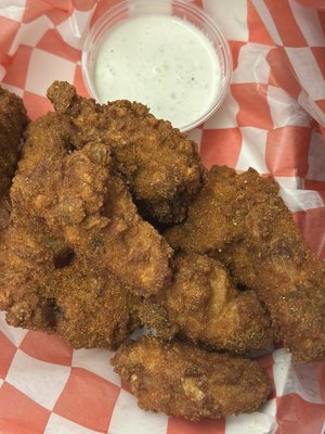 Close-up of crispy fried chicken wings in a red checkered basket with a side of white dipping sauce.