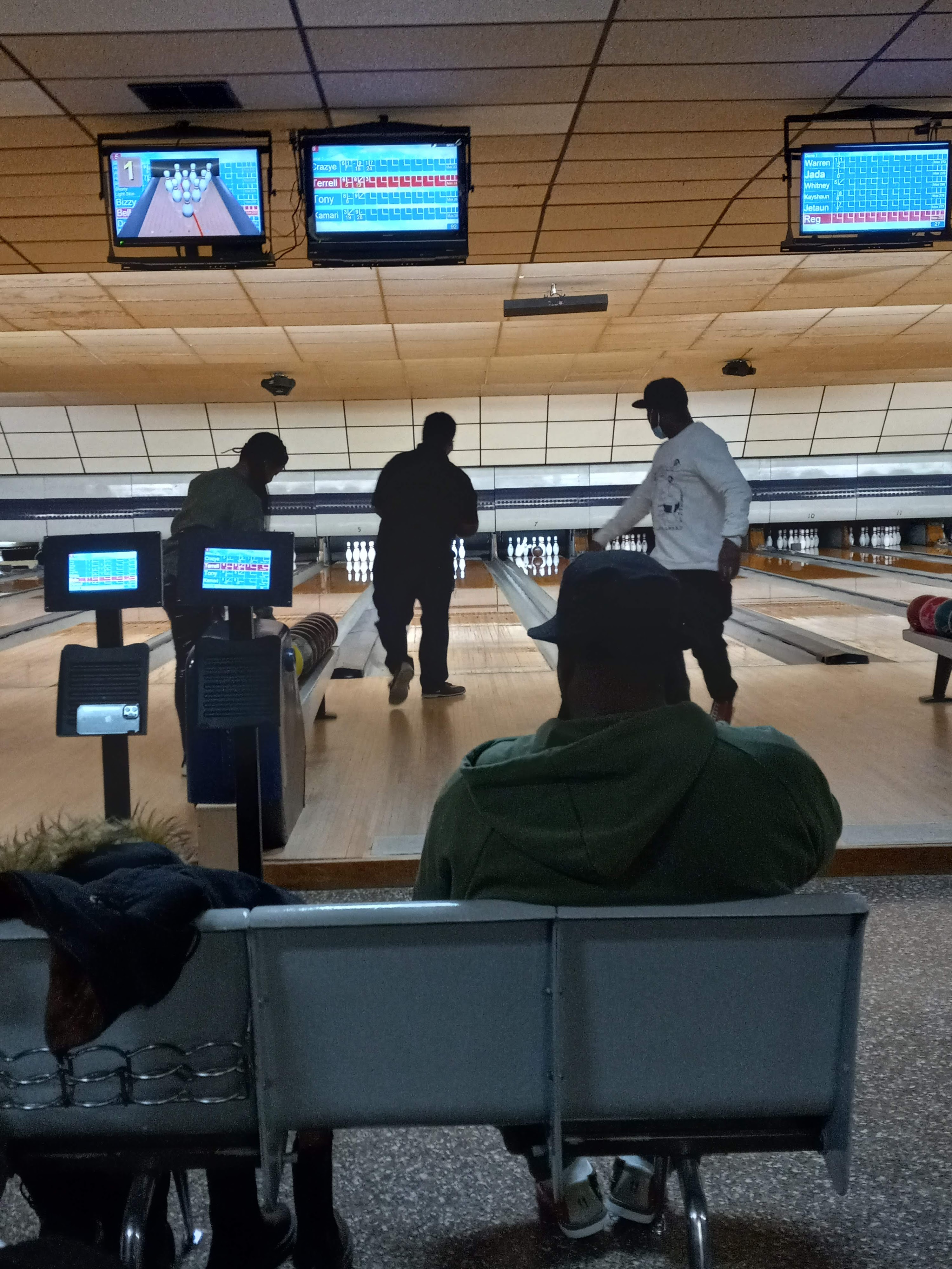 People bowling at an indoor alley with wooden lanes and overhead digital scoring monitors.