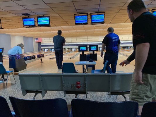 Several people bowling on lanes equipped with automatic scoring monitors and classic wood-look flooring.