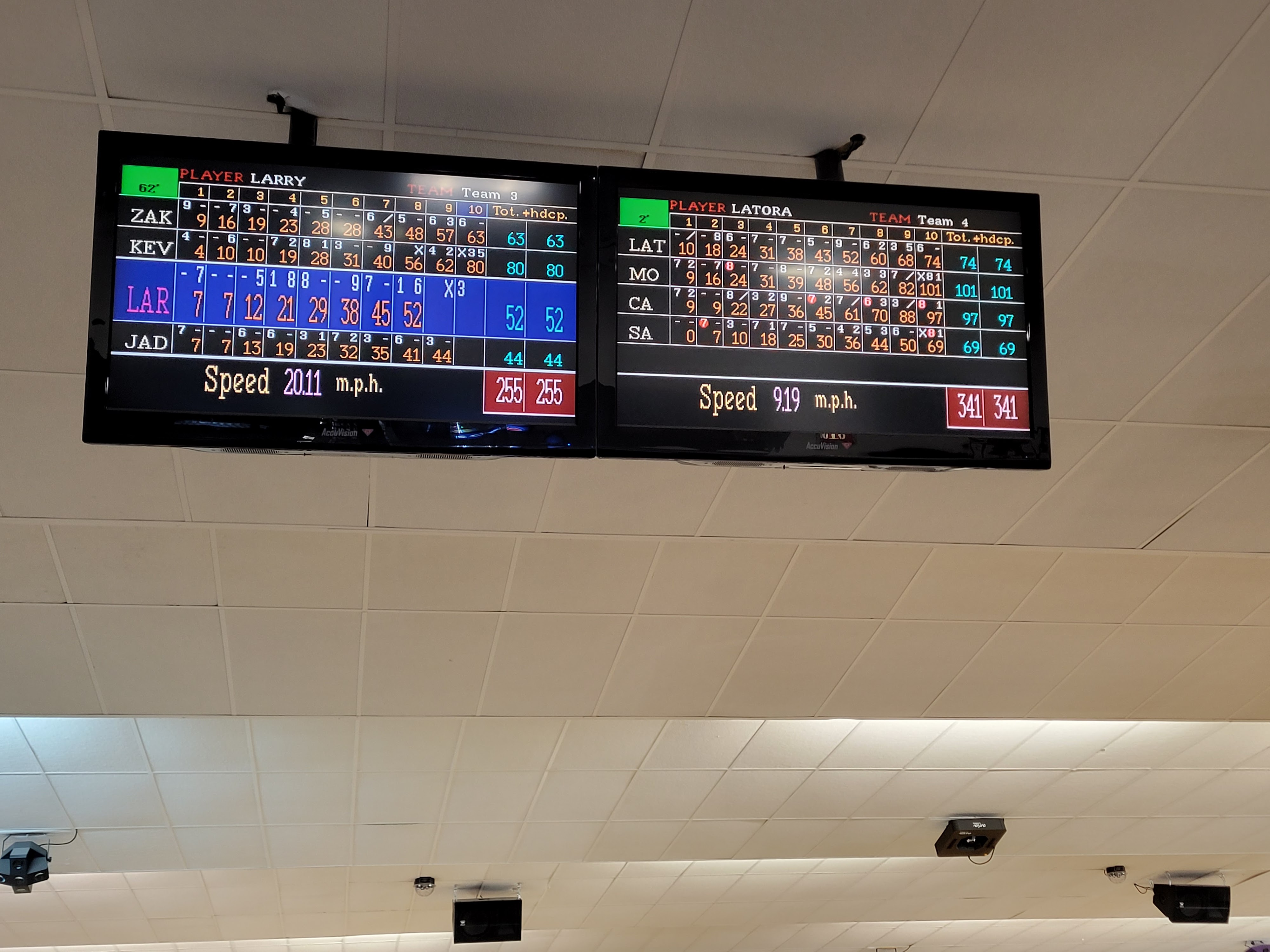 Close-up of two overhead digital bowling scoreboards showing player scores and ball speeds.