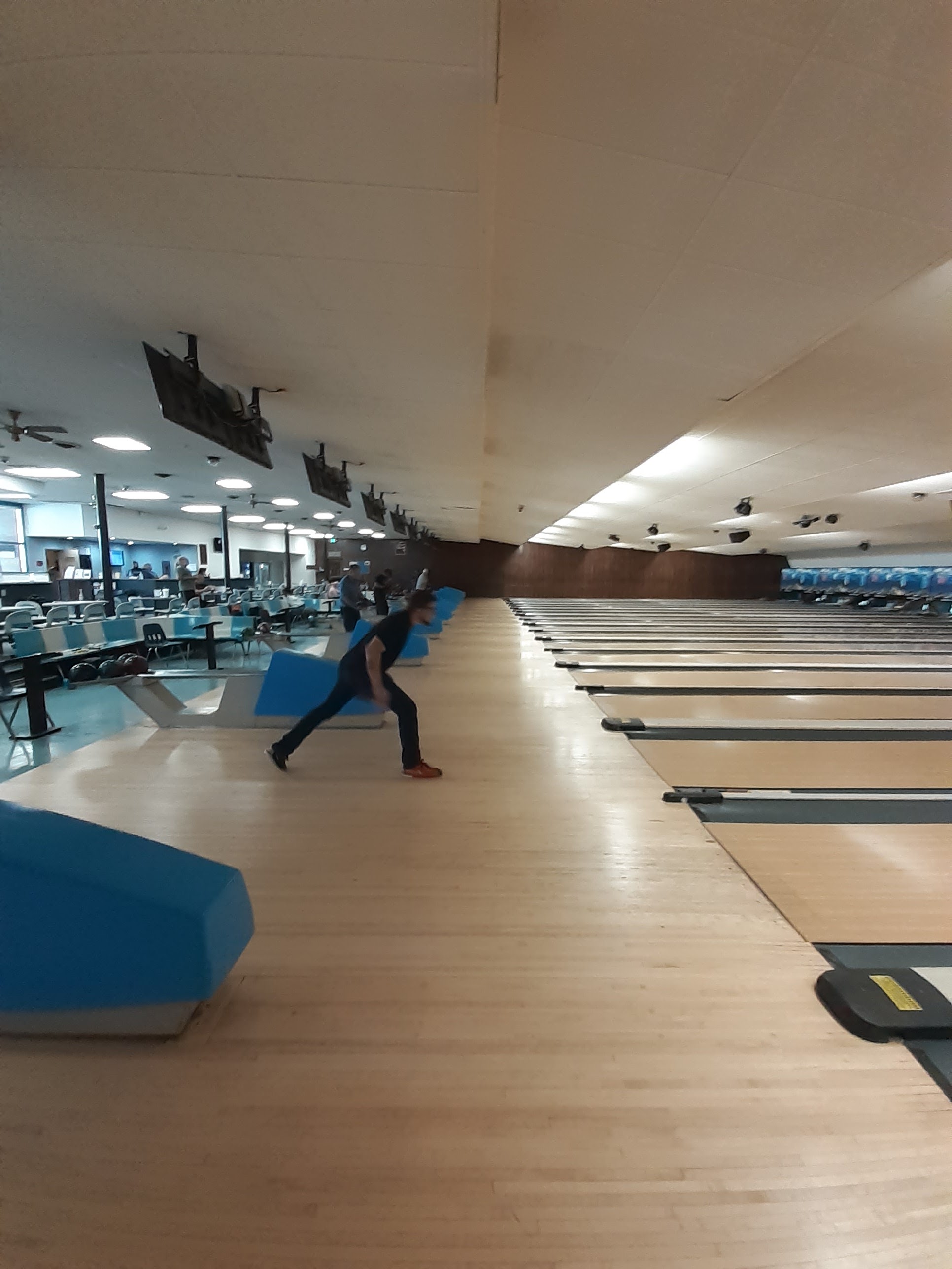 A person in mid-motion throws a bowling ball down a wooden lane at a bowling center.