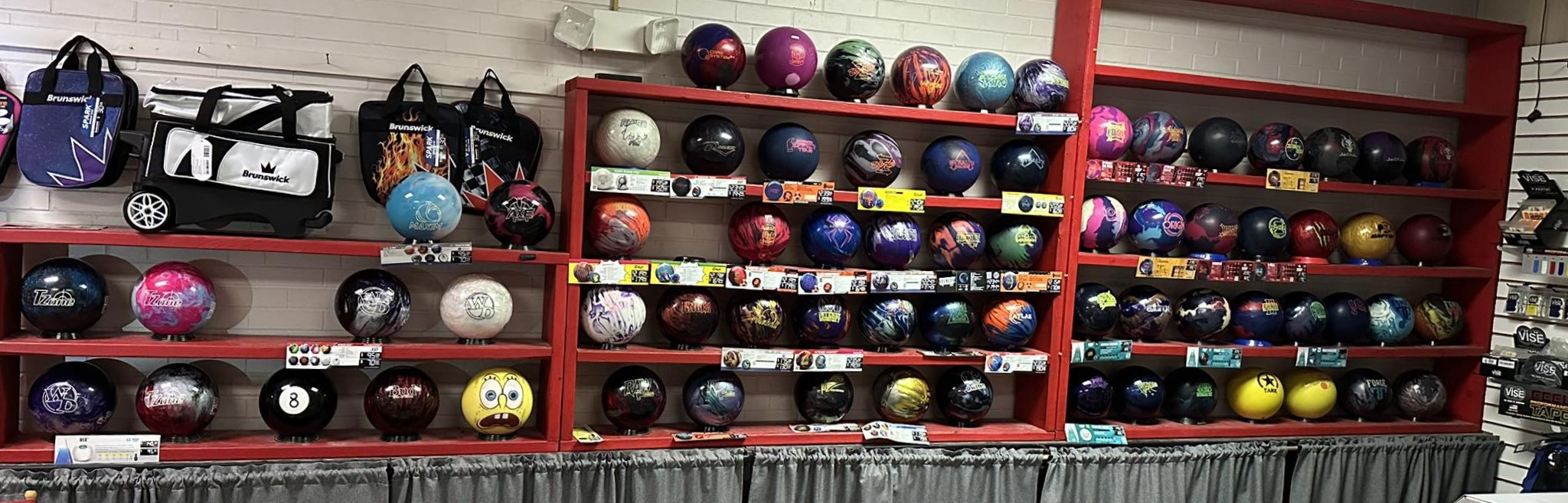 A wide retail display featuring rows of colorful professional bowling balls on red wooden shelves in a pro shop.