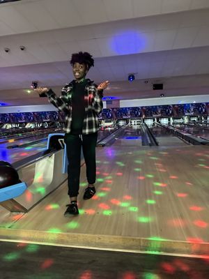 A person posing on a bowling lane approach during a cosmic bowling session with colorful light patterns on the floor.