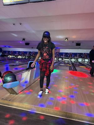 A woman smiling on a bowling lane during a cosmic bowling session with colorful light patterns on the floor.