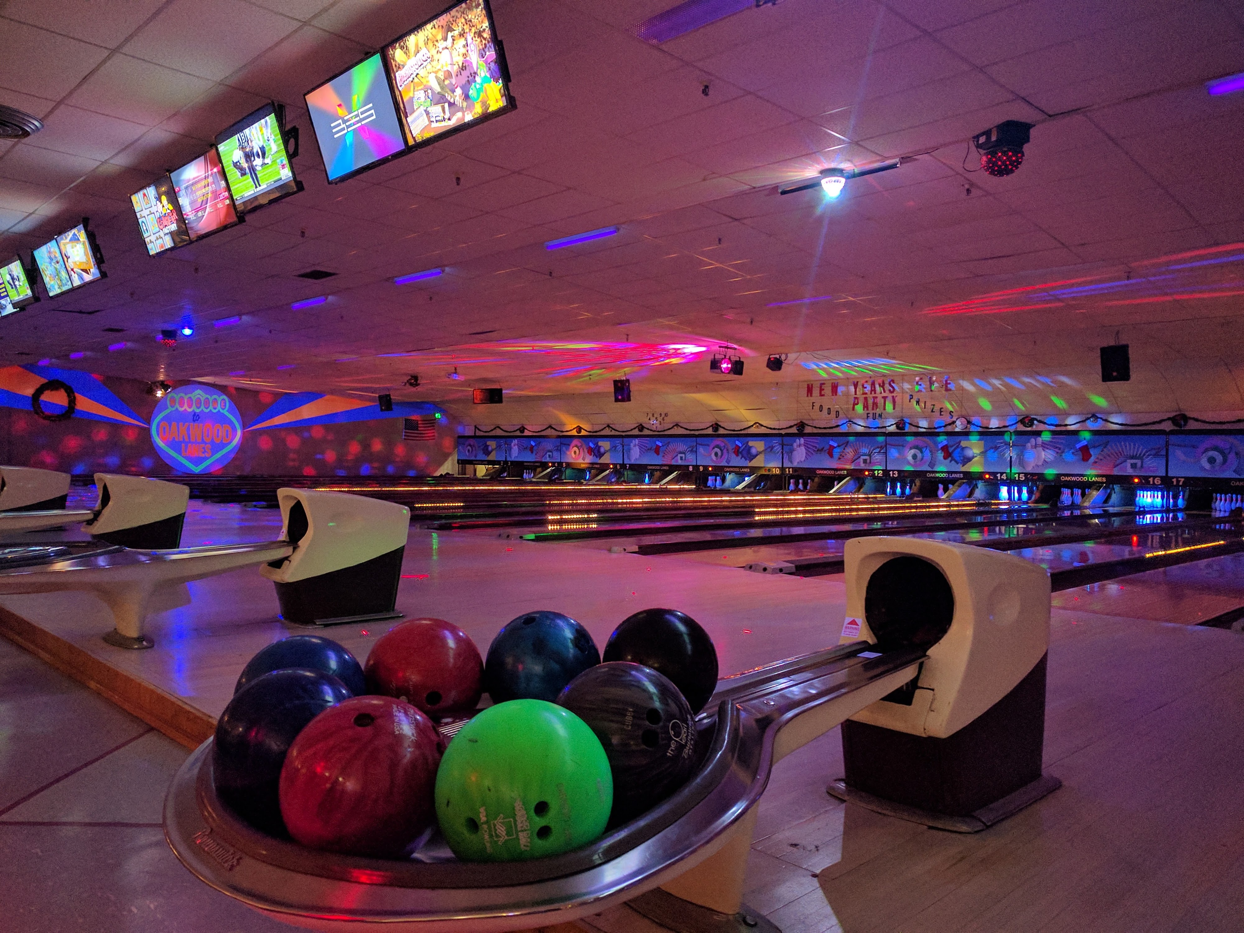 A bowling ball return filled with colorful balls under neon glow-in-the-dark lighting at Oakwood Lanes.