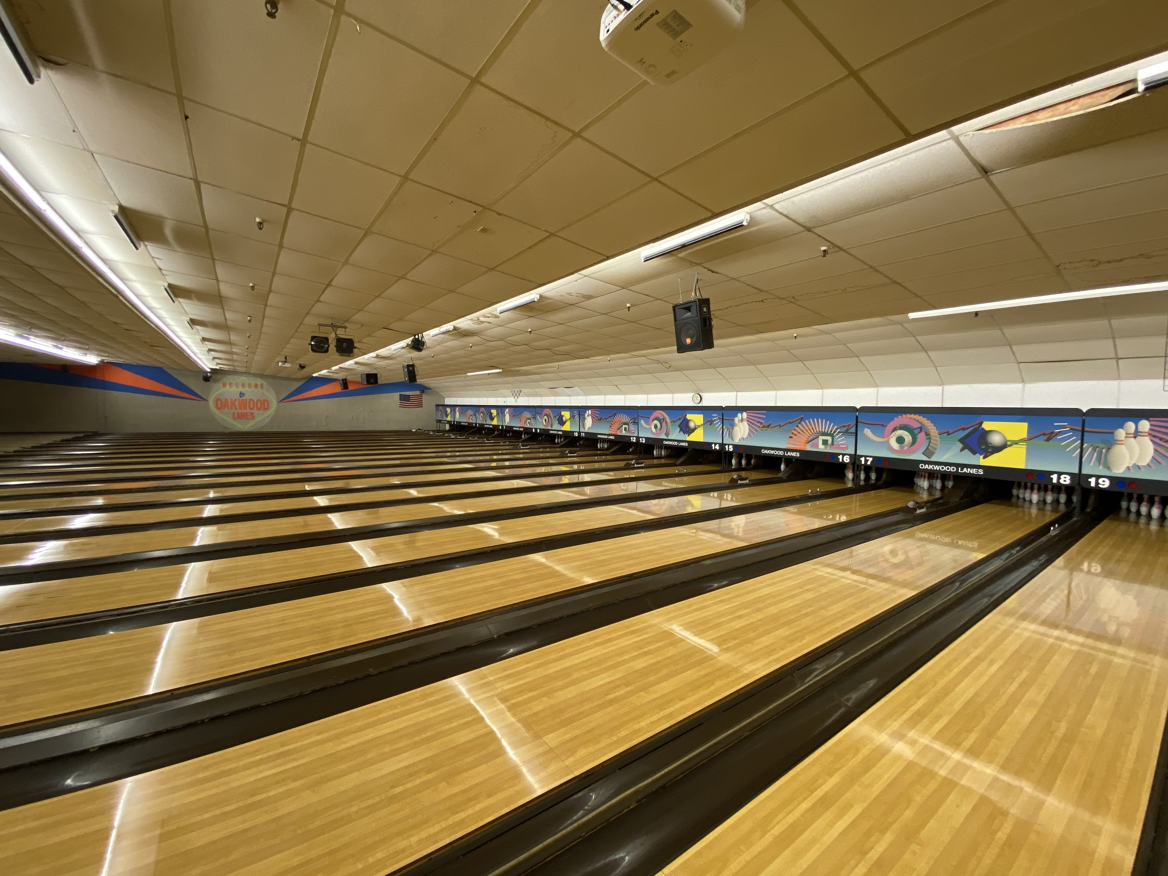 A wide view of nineteen polished bowling lanes at Oakwood Lanes with colorful masking units at the end.