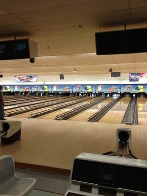 A wide view of multiple wood-grain bowling lanes with overhead scoring monitors and seating at Oakwood Lanes.