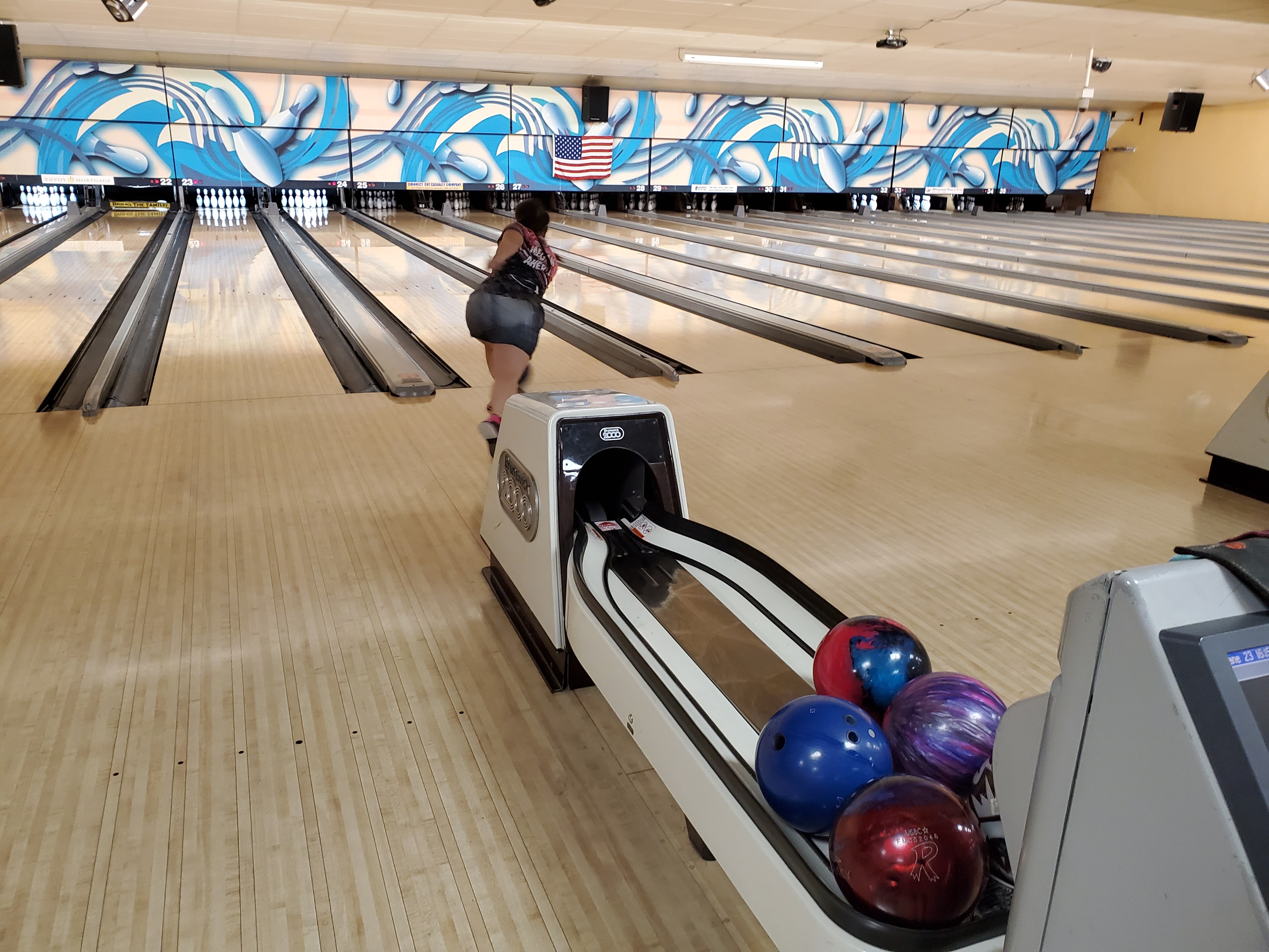 A person bowling on a lane at Apple Valley Bowl with colorful bowling balls in a foreground ball return.