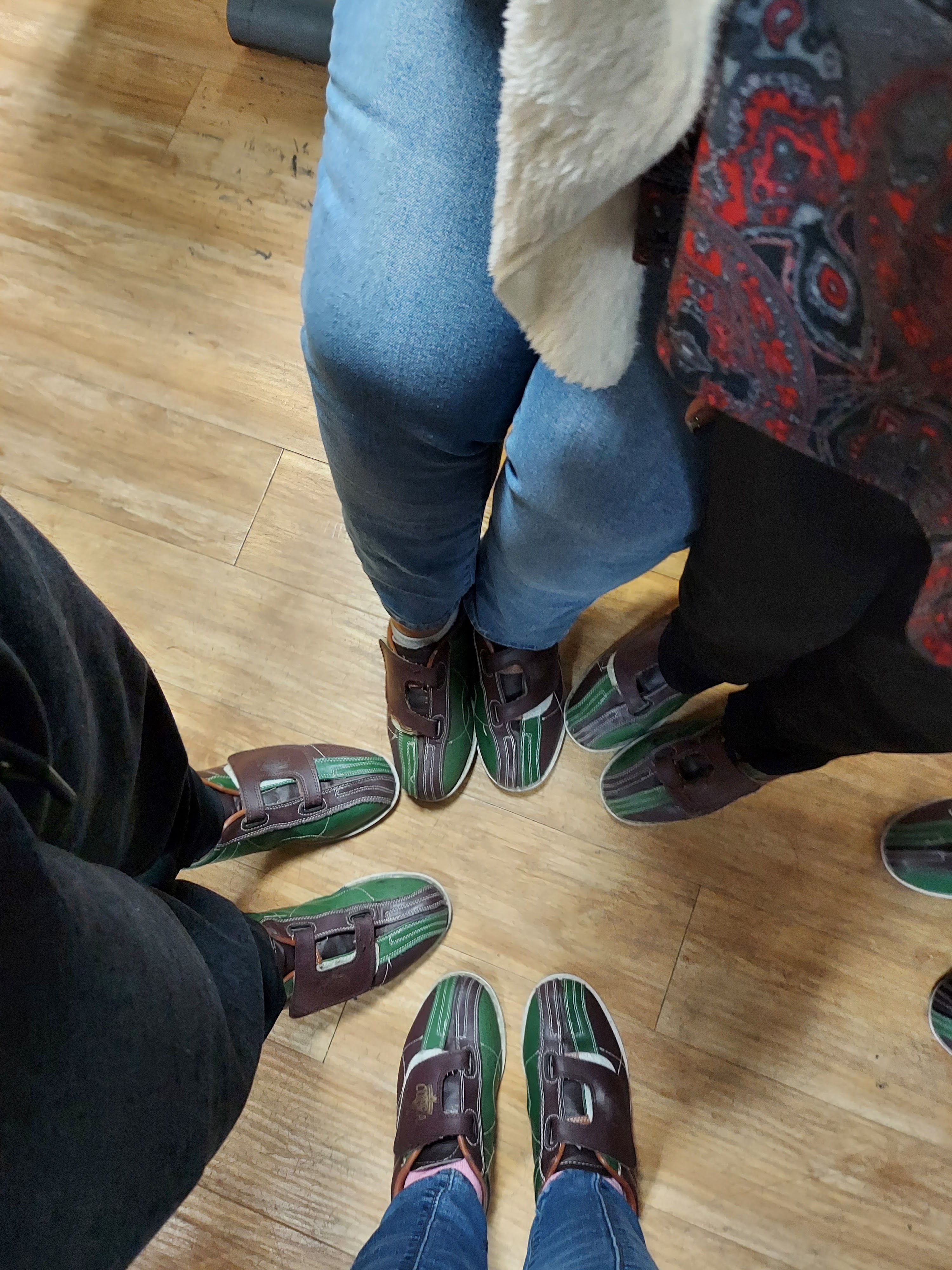 A top-down view of four people wearing green and brown rental bowling shoes standing in a circle.