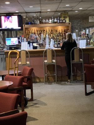 A customer sits at a wooden bar with a bartender behind the counter in a bowling alley lounge.
