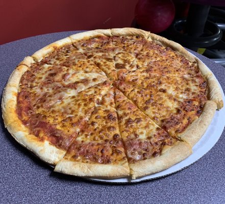 A whole cheese pizza sliced on a white cardboard tray atop a speckled table in a bowling alley.