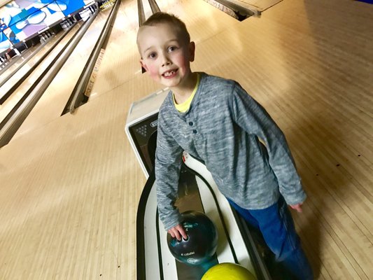 A smiling young boy standing next to a ball return on a bowling lane.