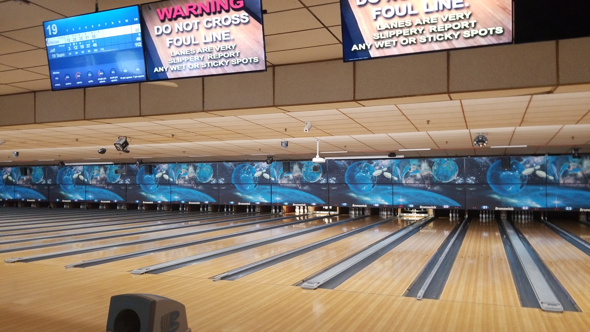 A wide view of multiple bowling lanes with digital scoring monitors overhead, displaying scores and foul line warnings.