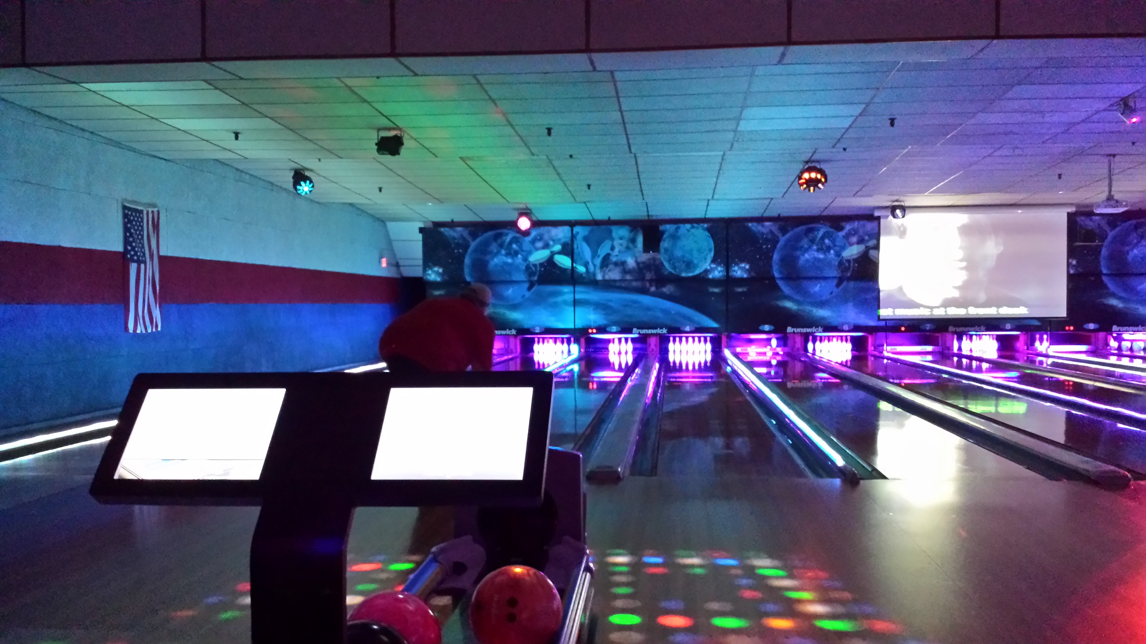 A cosmic bowling alley with purple and blue lights illuminating the lanes, showing a bowler and scoring screens.